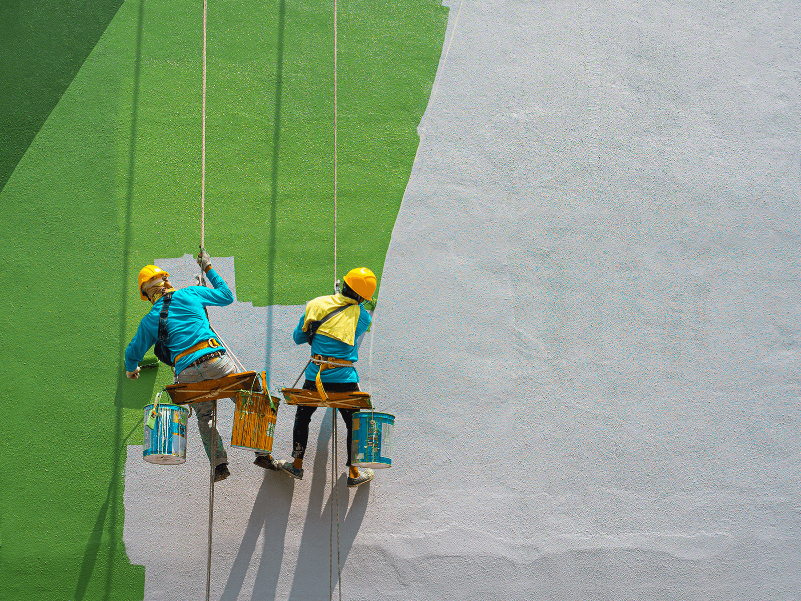 2 painters hanging from side of building